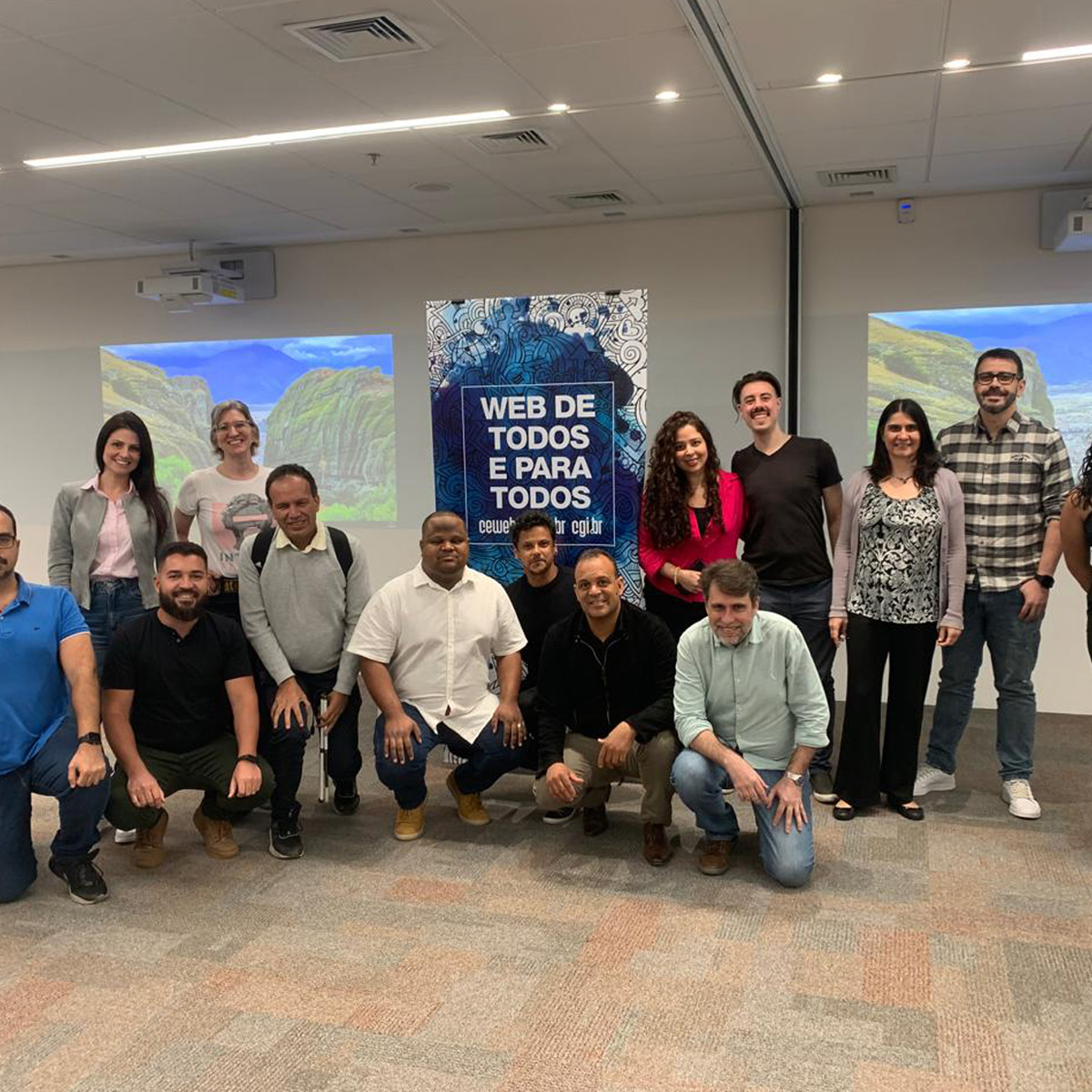 Equipe do Comitê da ABNT posa para foto em frente a dois painéis projetados na parede e uma placa que diz: Web de todos e para todos.