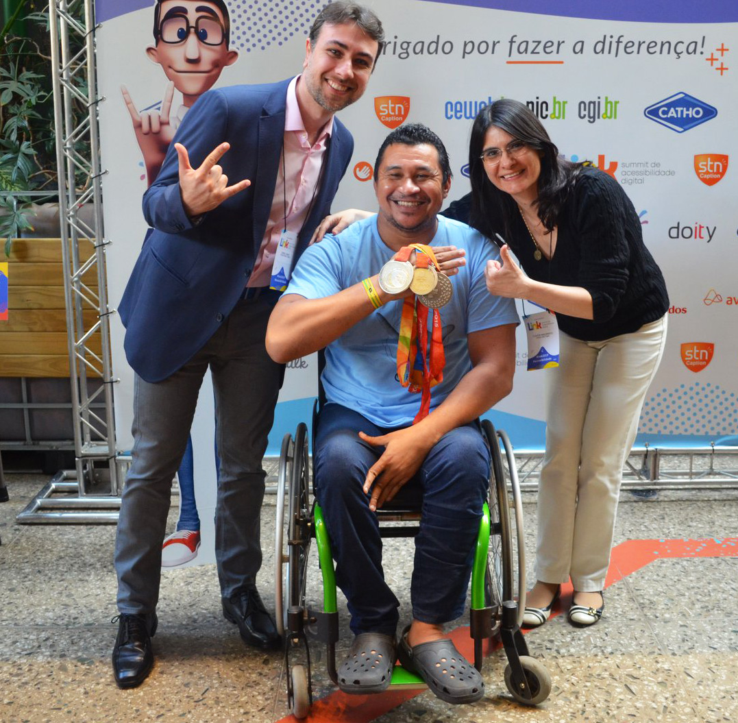 Foto de Rafael Vanzo e Cláudia Nascimento, co-fundadores da Acesso para Todos junto Clodoaldo segurando medalhas.